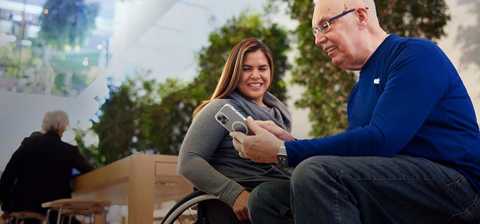 Tom oturuyor ve iPhone ile bir müşteriye yardımcı oluyor.