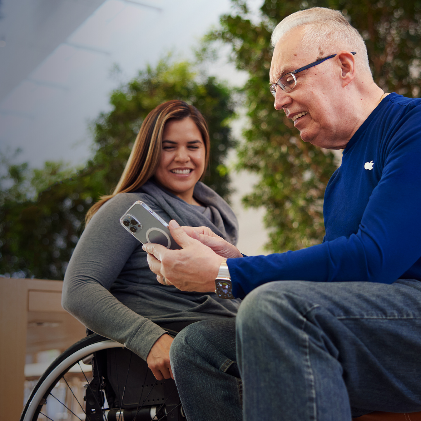 Tom oturuyor ve iPhone ile bir müşteriye yardımcı oluyor.