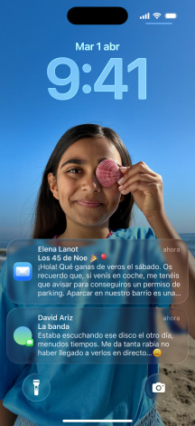 Cinco iPhone que se superponen ligeramente al que está al lado. El modelo más a la izquierda muestra una conversación con un fondo en Mensajes. El segundo modelo por la izquierda muestra la pantalla de inicio con iconos de apps en color. El modelo central muestra la pantalla de bloqueo con una foto de fondo, la hora en Liquid Glass y dos notificaciones en la parte inferior de la pantalla. El segundo modelo por la derecha muestra iconos de apps translúcidos en Liquid Glass. Y el modelo más a la derecha muestra el reproductor de música en Liquid Glass