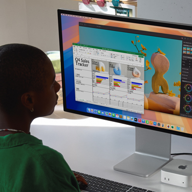 Woman working on an Excel spreadsheet on a Mac, sitting at a work table. The Excel spreadsheet is a Q4 sales tracker. Behind the Excel spreadsheet window is a Pixelmator Pro window.
