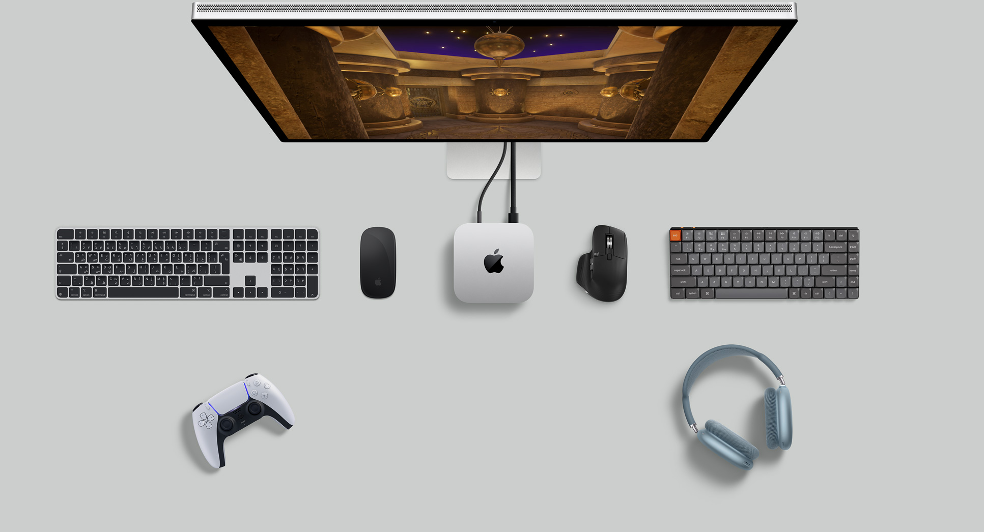 لقطة علوية لجهاز Mac&nbsp;mini فضي اللون ضمن إعداد مكتبي مع شاشة ولوحات مفاتيح لاسلكية وأجهزة ماوس لاسلكية ووحدة تحكم ألعاب وAirPods Max