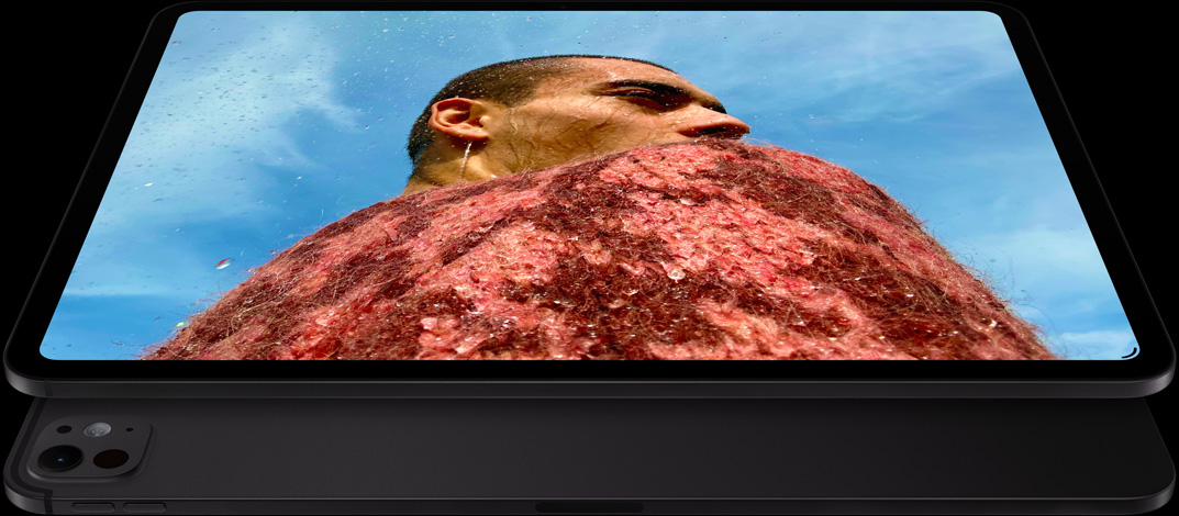 Un iPad Pro nero siderale in orizzontale visto di fronte, angoli arrotondati, cornice del display nera, display che mostra la foto di una persona con un maglione rosso sotto un cielo blu, al di sotto un altro iPad Pro nero siderale in orizzontale visto da dietro, sistema di fotocamere pro, tasto per alzare il volume, tasto per abbassare il volume