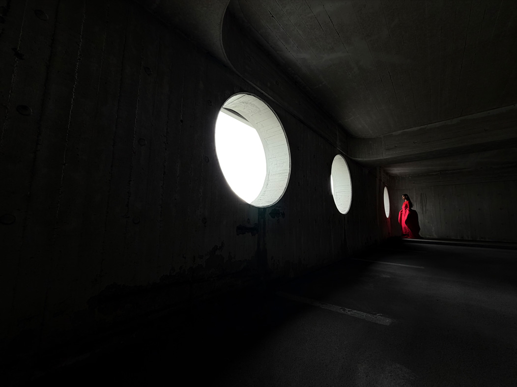A woman wearing a long red dress stands in an empty room being photographed. The Photo app toggles through the following focal lengths to demonstrate the capabilities of the pro camera system: 200 mm, 100 mm, 48 mm, 35 mm, 28 mm, 13 mm, and macro